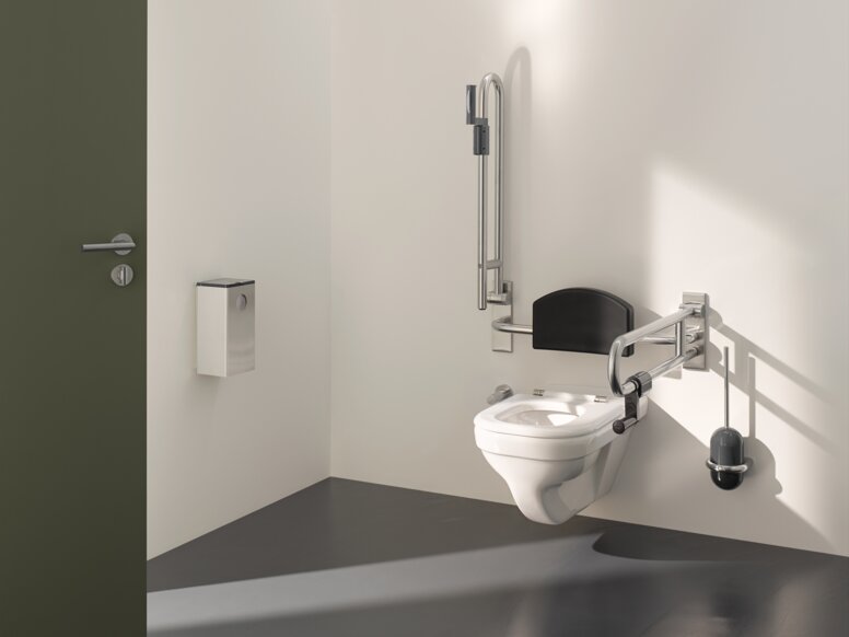 Barrier-free WC in public areas equipped with folding support handles, back support and toilet brush