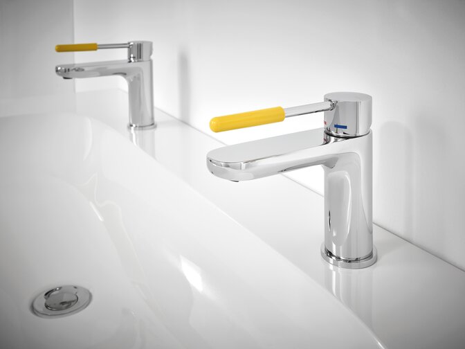 Two taps on a white washbasin with yellow handles